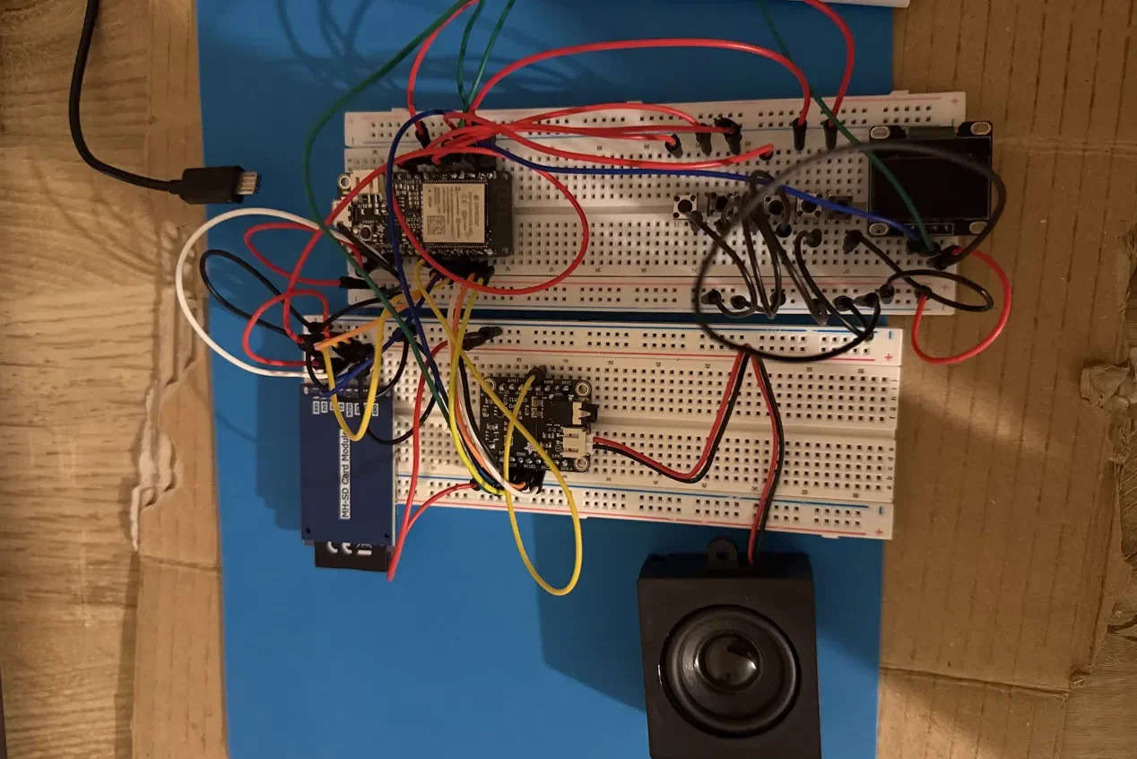 The working prototype across two breadboards, seen from above: an SD card module, an amplifier, the main board, push buttons, a small screen and a speaker, joined by jumper wires